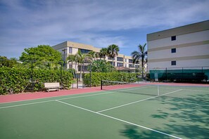 An outdoor tennis court with a net, surrounded by greenery and a building in the background. - Kings Crown 111 (Sanibel)