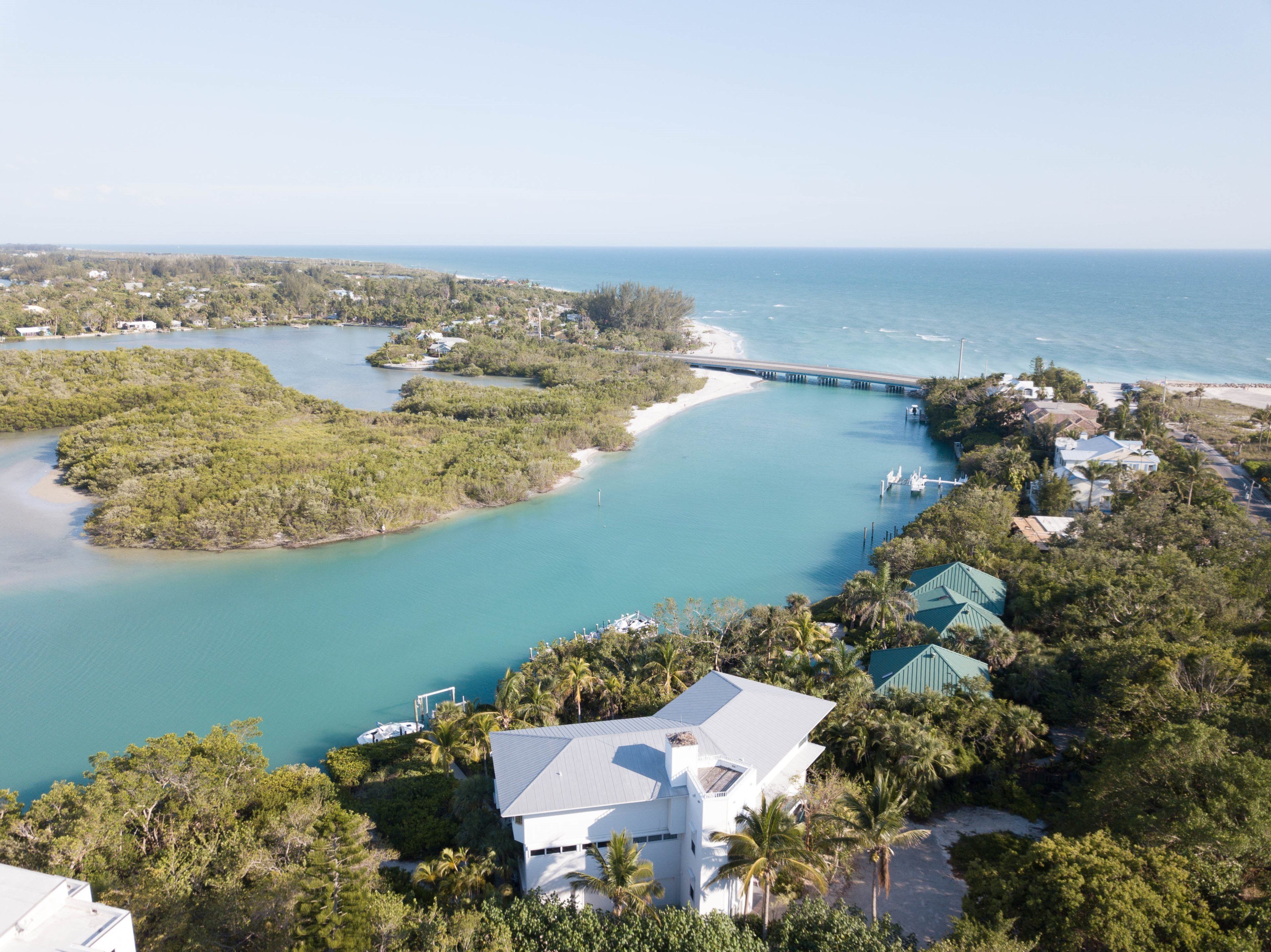 An aerial view of a coastal property with a large house, a dock, and a bridge connecting to a beach.
