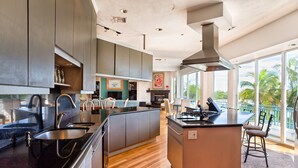 A modern kitchen with a central island, built-in cabinets, and a large window overlooking a balcony. - Sea Otter (Captiva)