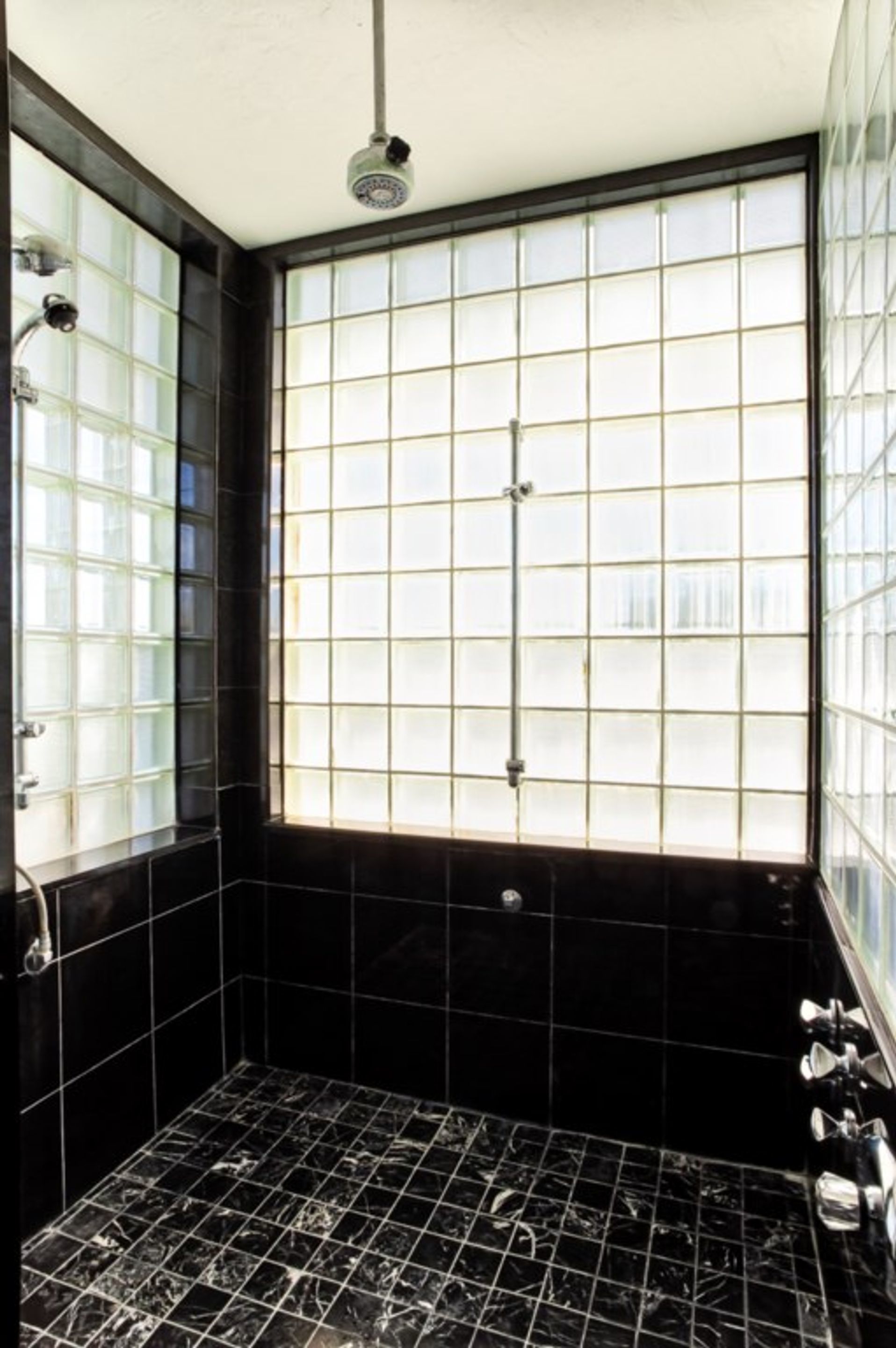 Ein Badezimmer mit großem Fenster, schwarzen Fliesenwänden und einer Duschkabine.