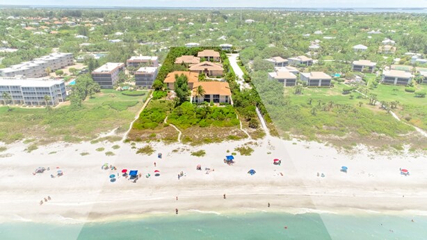 Luchtbeeld van een resort met een centraal gebouw, omgeven door weelderige begroeiing, een strand en diverse strandvilla's.