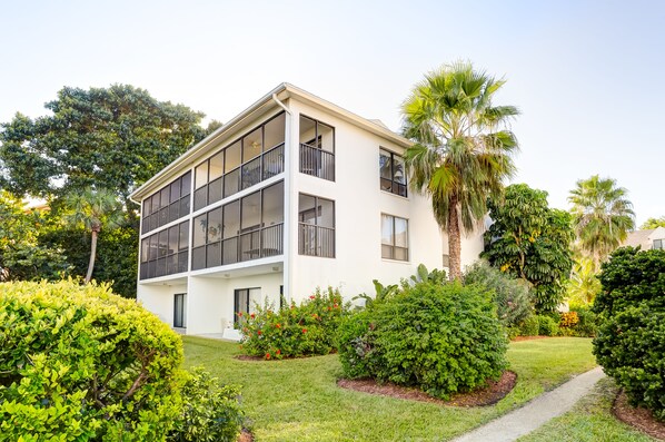 A modern two-story building with large windows and balconies, surrounded by well-maintained gardens and palm trees.