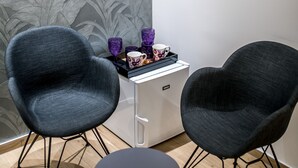 Habitació moderna amb dues cadires fosques, una taula rodona petita i un moble blanc amb tasses i una tassa de color morat.