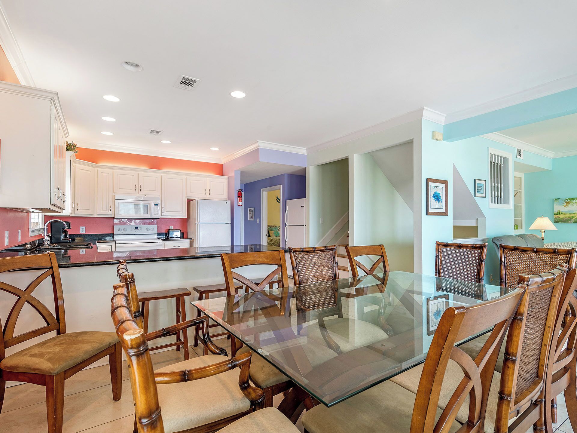 A modern kitchen with white cabinets, a central island, and a dining area with glass-top table and wooden chairs.