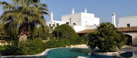 A swimming pool with a clear blue water, surrounded by greenery and white buildings in the background.