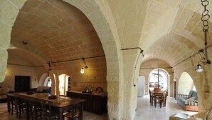 A spacious interior with high stone arches, a central dining area with a long table and chairs, and a cozy seating area with cushions. - Masseria La Brunetta (Massafra)