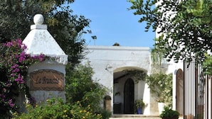 A stone pathway leading to a white building with an arched entrance, surrounded by potted plants and a sign reading "La Brunetta". - Masseria La Brunetta (Massafra)