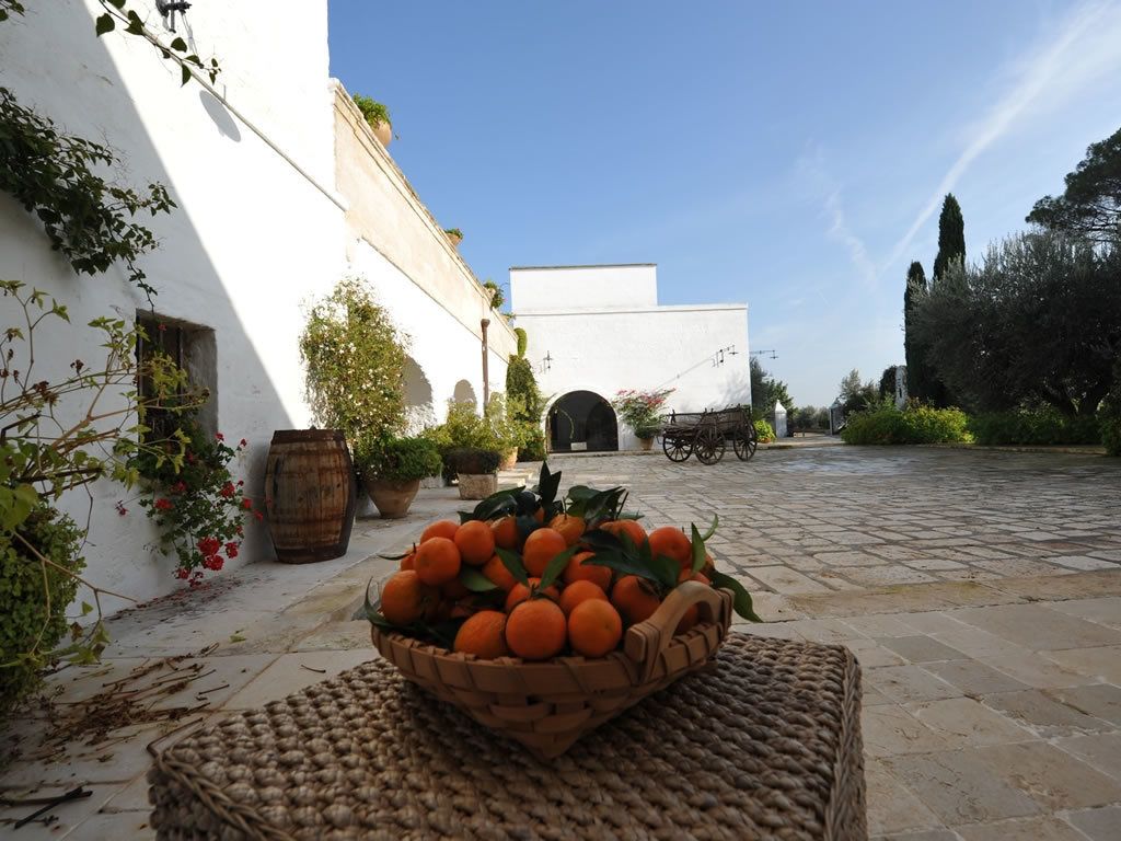 A courtyard with a basket of oranges, a white building, and a cart in the background.