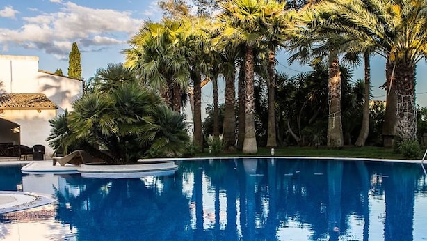 A swimming pool surrounded by palm trees and a building with a tiled roof. - Masseria La Brunetta (Massafra)