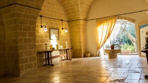 A spacious room with arched brick walls, a stone floor, a wooden bench, and a large window with curtains. - Masseria La Brunetta (Massafra)