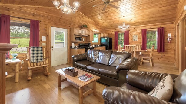 A wooden cabin interior with a living room, kitchen, and dining area.