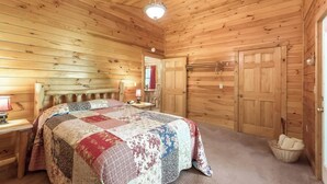A wooden-paneled bedroom with a large bed, a nightstand, a lamp, and a door leading to another room.
