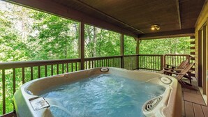 A hot tub on a wooden deck with a view of a forest.