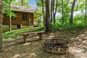 A rustic cabin with a wooden exterior, a bench, and a metal fire pit in a forested area. - Whispering Pine: Cozy Cabin with Hot Tub & Views (Logan)