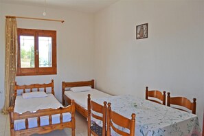 Um quarto com duas camas de madeira, uma mesa de jantar com cadeiras, uma janela com cortinas e uma pequena imagem na parede.