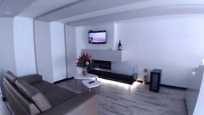 Un salon moderne avec un canapé, une table basse, un téléviseur à écran plat fixé au mur et une cheminée.