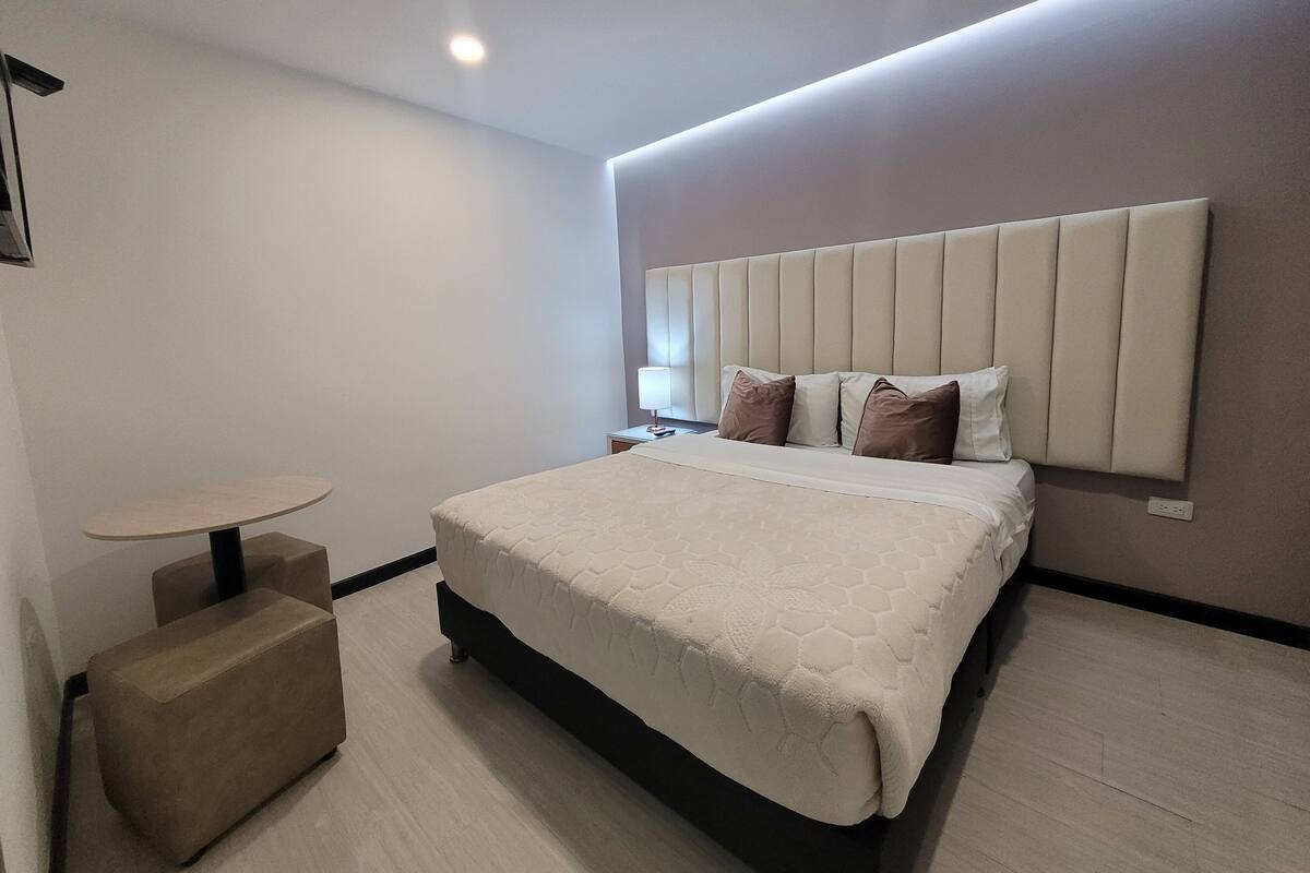 Ein modernes Hotelzimmer mit einem großen Bett, einem Nachttisch und einem kleinen runden Tisch.