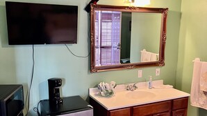 Ein Badezimmer mit Waschbecken, Spiegel und einem an der Wand befestigten Fernseher.