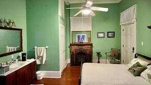 Ein Schlafzimmer mit Bett, Deckenventilator, Kamin und einem Badezimmer mit Waschbecken und Spiegel.