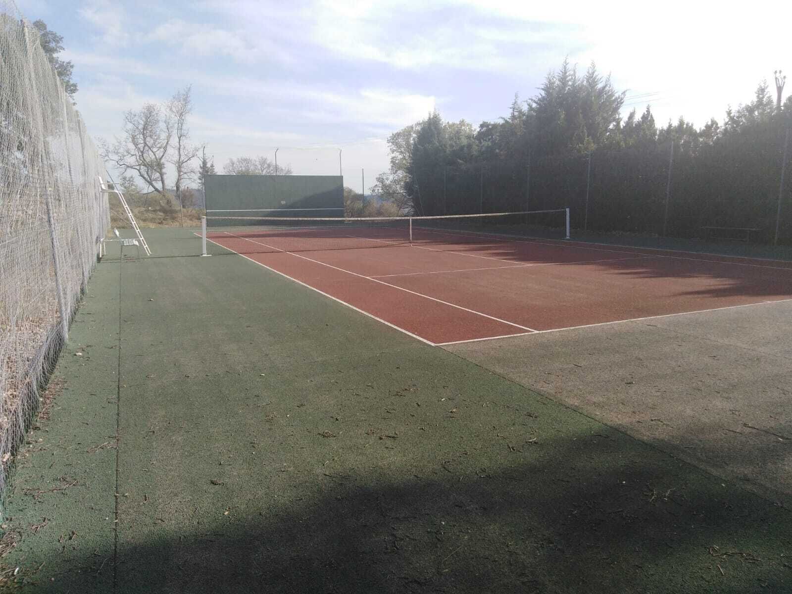 Una cancha de tenis con una red, rodeada por una valla y árboles.