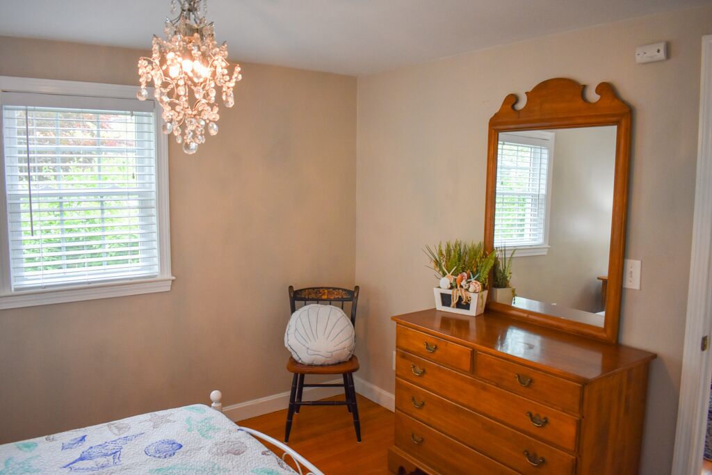 A bedroom with a wooden dresser, a mirror, a chair, and a chandelier.