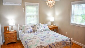 A bedroom with a bed, bedside tables, a chandelier, and a window with blinds. - Lovely three bedroom home with access to Swan Pond (Dennis Port)