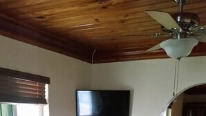 A room with a wooden ceiling, a flat-screen TV mounted on the wall, a small wooden table, and a glass-top coffee table. - 2 Bedroom 2bath cottage (Freeport)