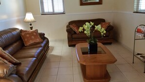 A living room with a brown leather sofa, a wooden coffee table, and a potted plant. - 2 Bedroom 2bath cottage (Freeport)