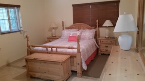 A bedroom with a wooden bed, bedside tables, a nightstand, a lamp, and a window with blinds. - 2 Bedroom 2bath cottage (Freeport)