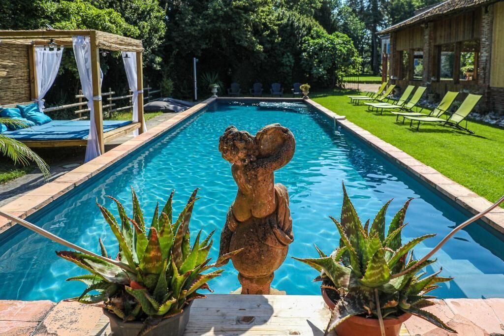 A pool with a statue, a gazebo, and lounge chairs.