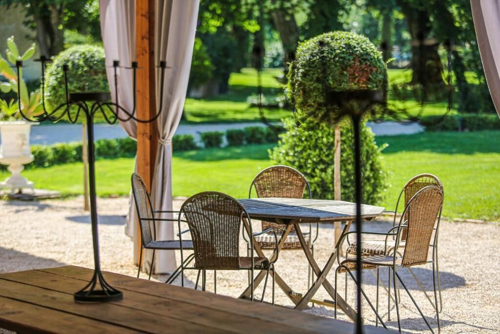 An outdoor patio with a table and chairs, surrounded by greenery and a well-maintained garden.