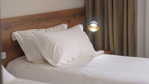 Et hotelværelse med en træsenggavl, to senge med hvide sengetøj, en natlampe og beige gardiner.