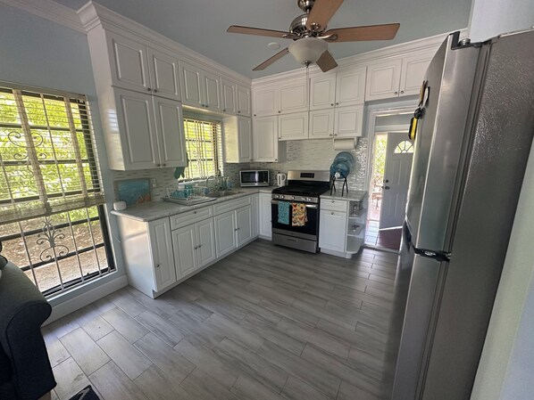 A modern kitchen with white cabinets, a stainless steel refrigerator, a microwave, and a stove. - Ms. Kay's Cottage, in Lucaya near to beach and Port Lucaya (Freeport)
