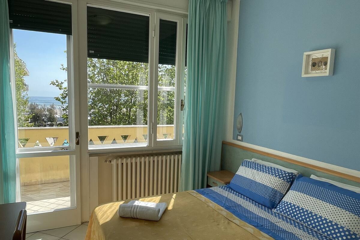 A bedroom with a bed, a window, a radiator, and a view of the outside.