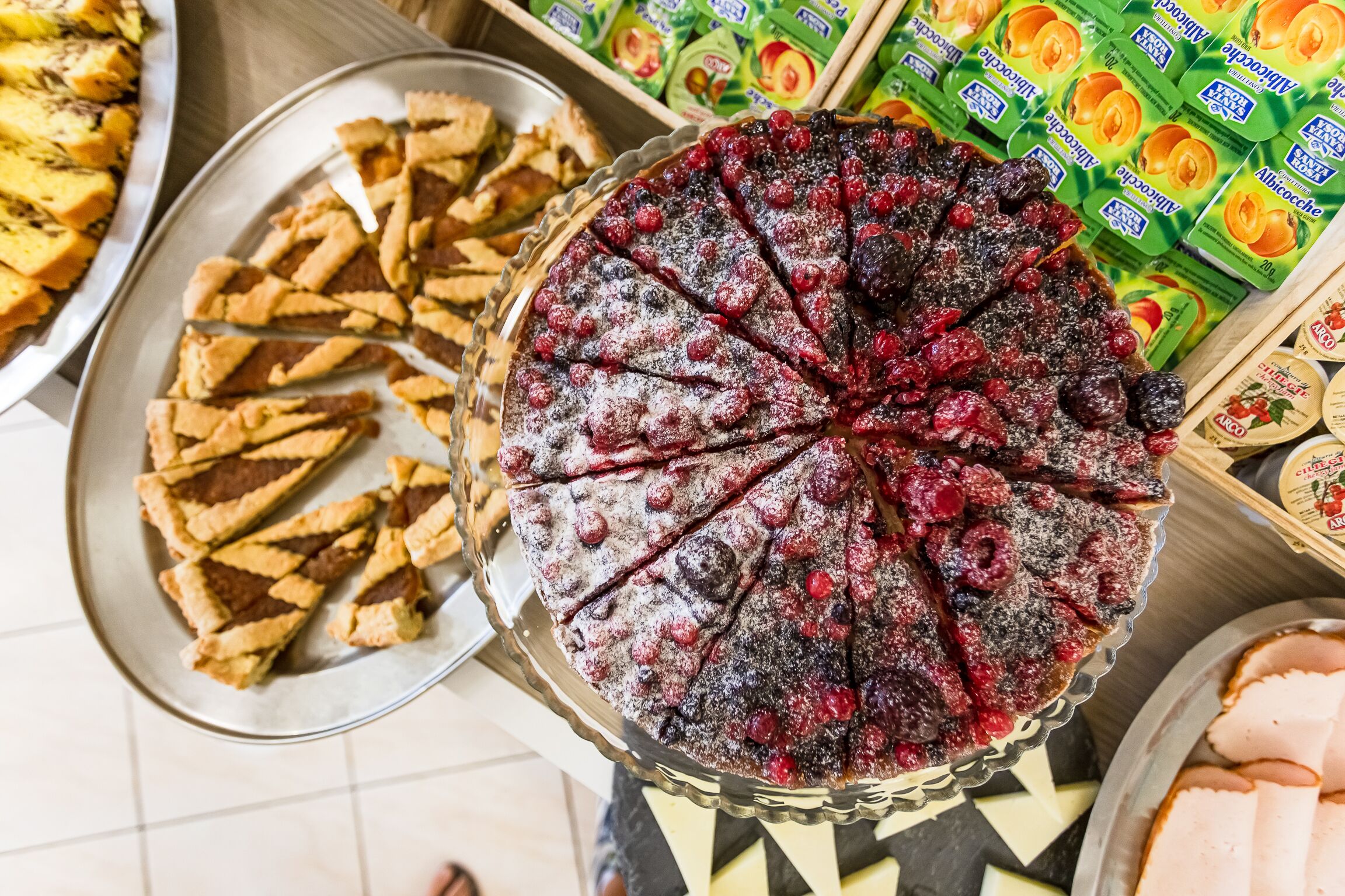 Una varietà di dolci su un tavolo del buffet, tra cui una torta con frutti di bosco e un vassoio di pasticcini.