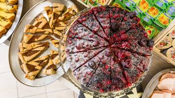 Una varietà di dolci su un tavolo del buffet, tra cui una torta con frutti di bosco e un vassoio di pasticcini.