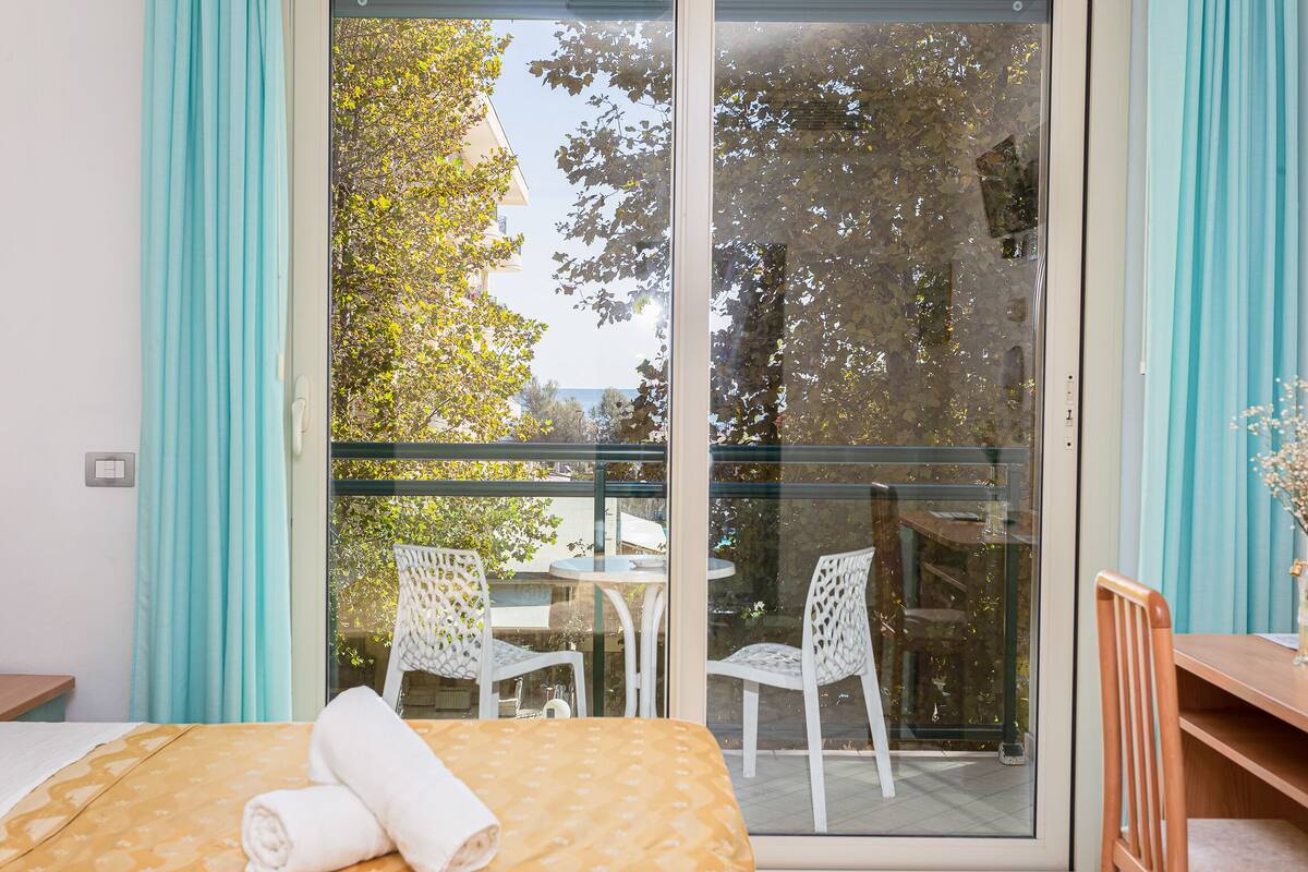 A room with a bed, a table, and chairs, a sliding glass door leading to an outdoor area with a table and chairs.