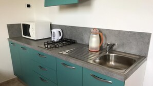 A kitchen with teal cabinets, a microwave, a gas stove, a kettle, and a sink. - Maison de Charme Iommella (Sant'Agnello)