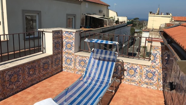 A rooftop terrace with a blue-striped lounge chair, tiled walls, and a view of the city. - Maison de Charme Iommella (Sant'Agnello)