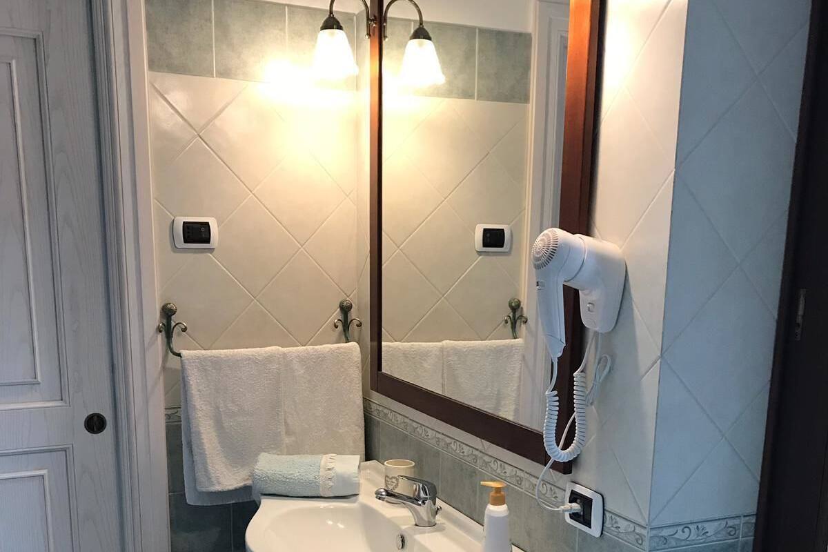 Ein Badezimmer mit einem weißen Waschbecken, einem Spiegel, einem Föhn und einem Handtuchhalter.