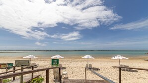 A beach with umbrellas and a signboard. - Cobertura com Piscina Privativa | Pé na Areia | Vista Mar | Barra Bali | Destino BSM 417 (Barra de São Miguel)