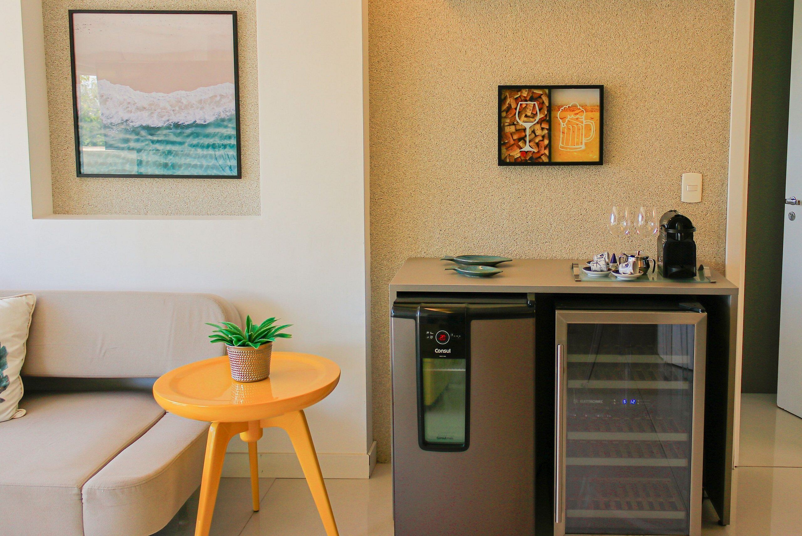 A compact kitchenette with a refrigerator, a coffee maker, and a small table with a plant.