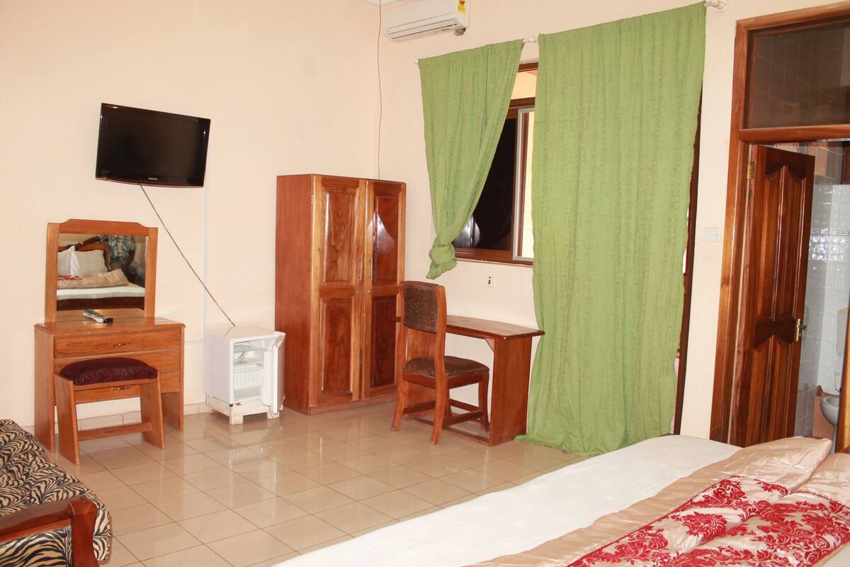 Une chambre à coucher comprenant un lit, un bureau en bois, une chaise, une télévision et une armoire.