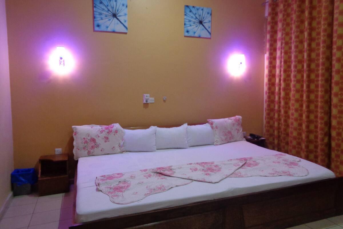 Une chambre à coucher avec un lit, deux lampes fixées au mur et une fenêtre avec des rideaux.