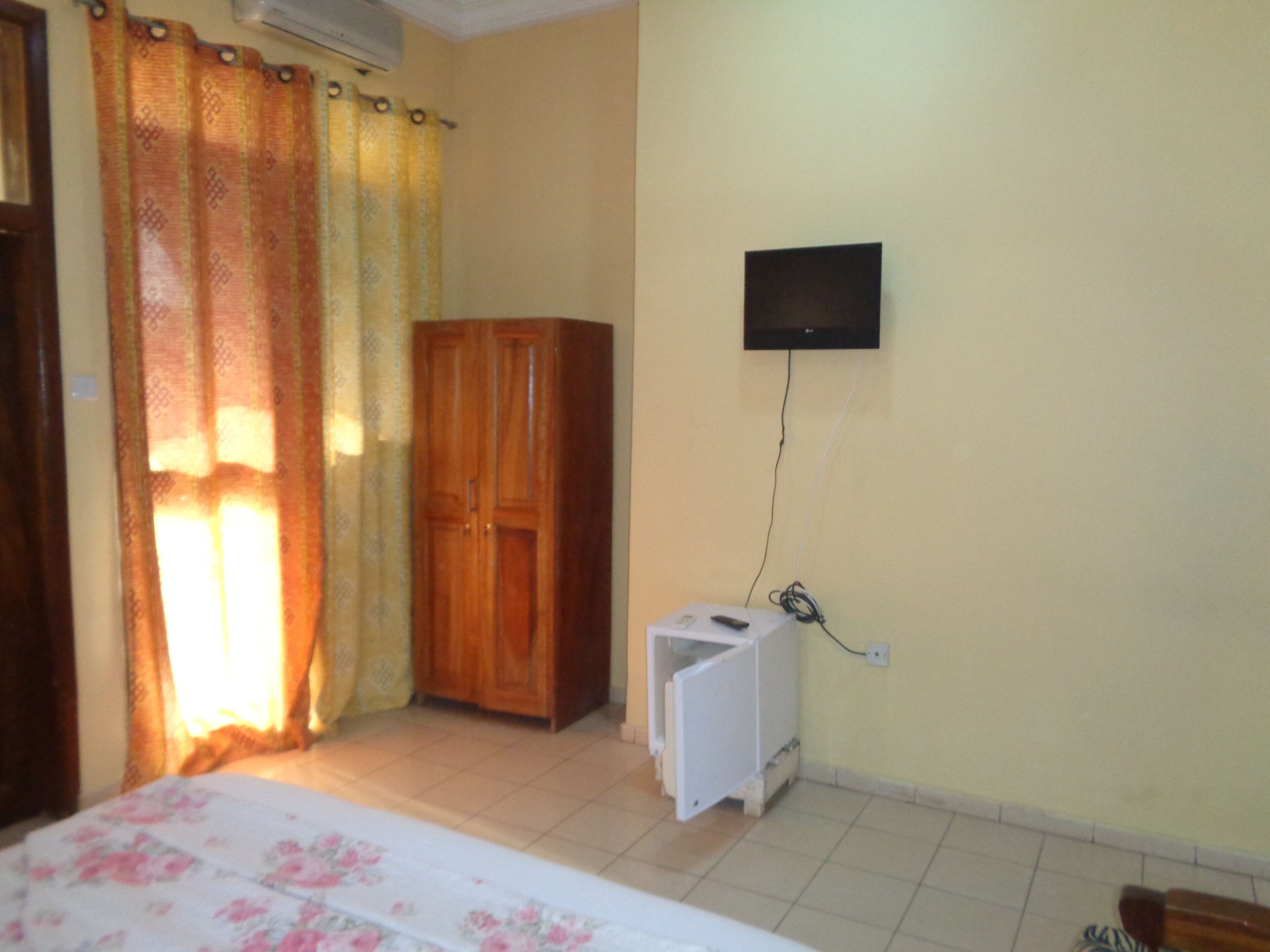 Une chambre comprenant un lit, une armoire, un téléviseur fixé au mur et un petit meuble blanc.