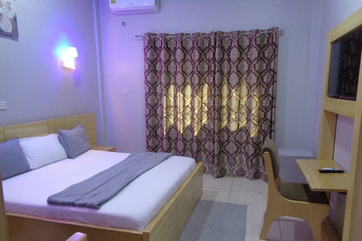 Une chambre à coucher avec un lit, une table de chevet et un téléviseur posé sur un meuble.