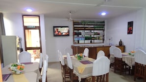 A dining area with tables set for a meal, chairs with white covers, a bar area with bottles, and a television on the wall. - Queensland Hotel (Sekondi-Takoradi)