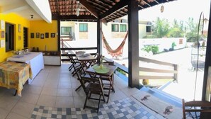 A covered outdoor dining area with tables and chairs, a small table with a tablecloth, and a hammock. - Pousada Carcará (Ipojuca)