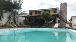 A swimming pool with lounge chairs and a staircase leading to a building with a stone facade. - Pousada Carcará (Ipojuca)
