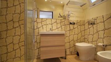 A bathroom with a patterned tile wall, a glass shower enclosure, a white sink, and a toilet.
